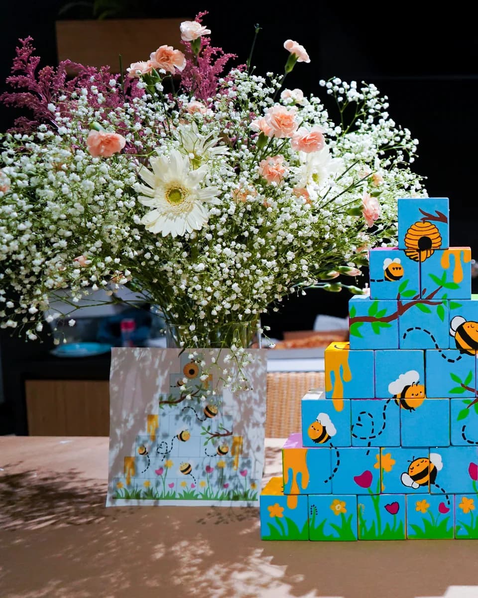 Mural colectivo de cubos pintados con abejas y flores, montado en un baby shower