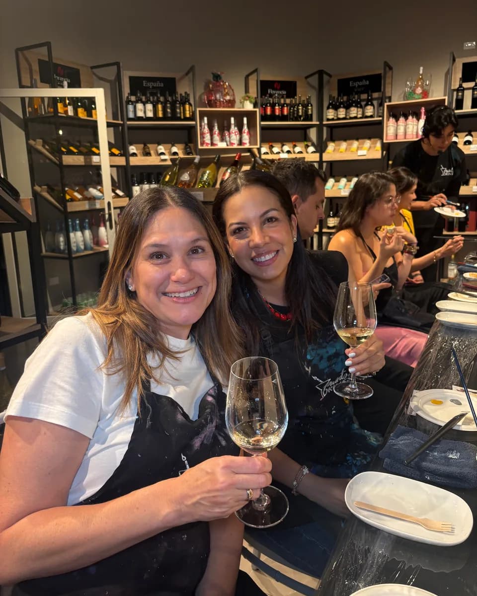Dos amigas brindan con vino frente a sus lienzos en un Maridaje Artístico en una vinoteca