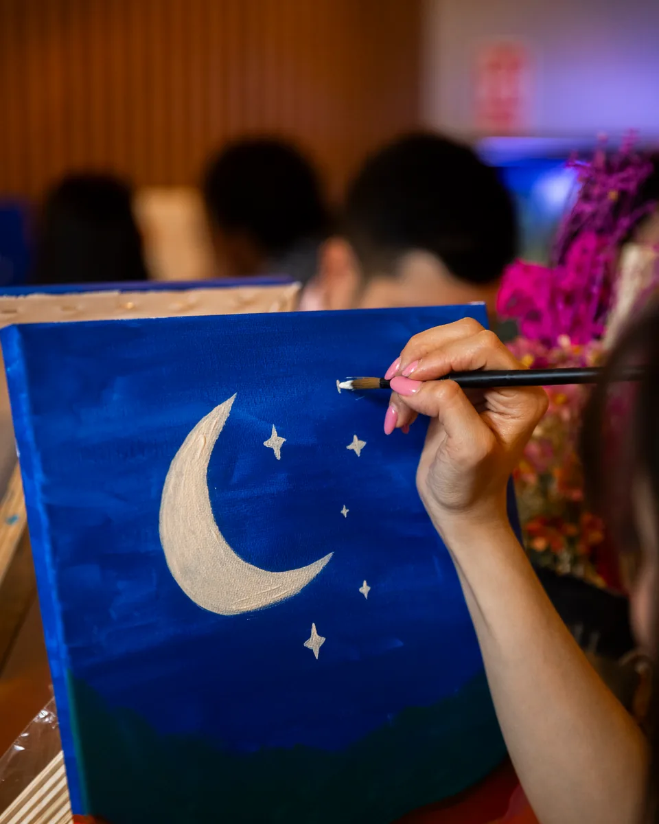 Lienzo de una luna con estrellas sobre montañas, pintado paso a paso en un Paint Night
