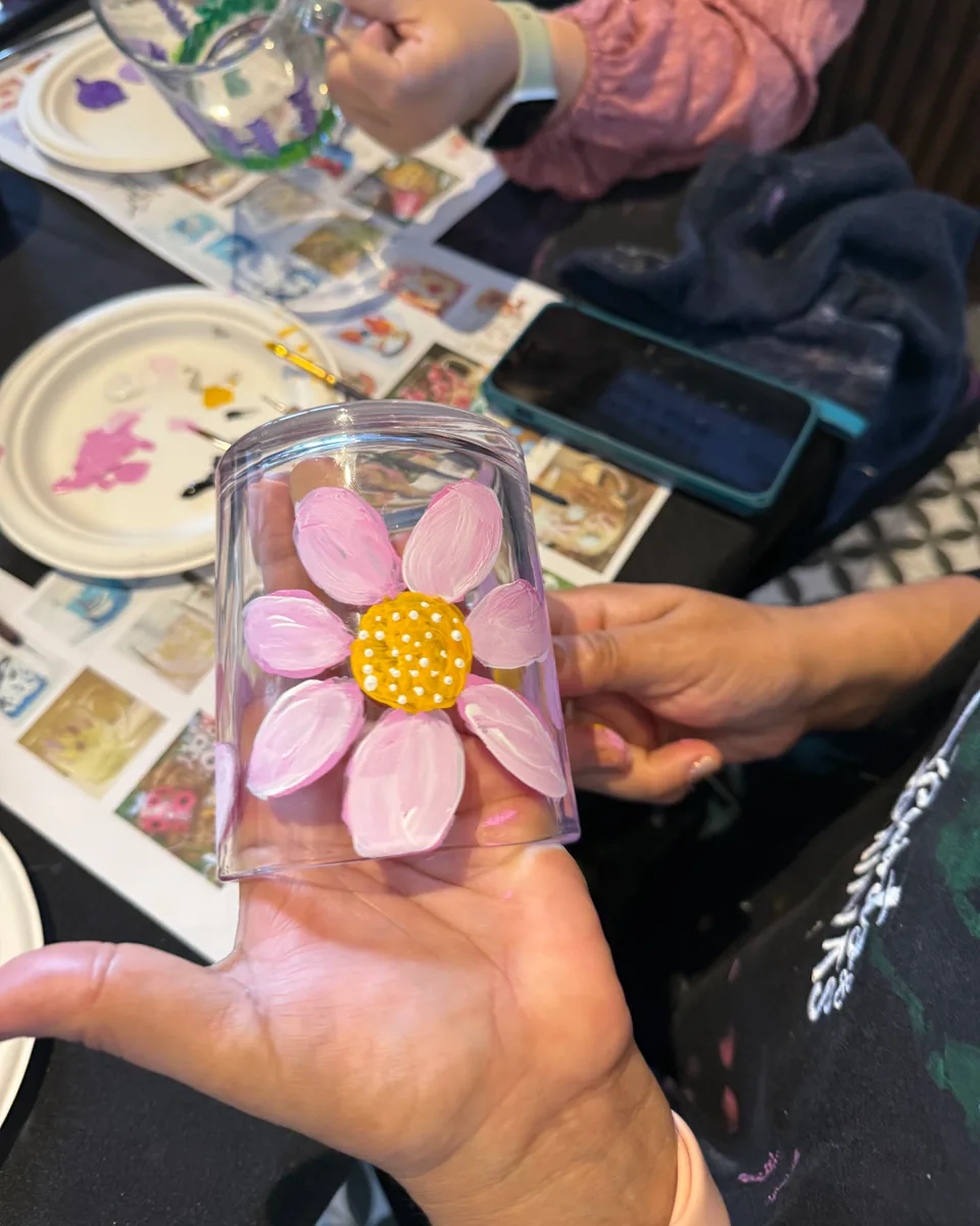 Taza de vidrio pintada a mano con una flor rosada en una sesión de Pinta tu Taza