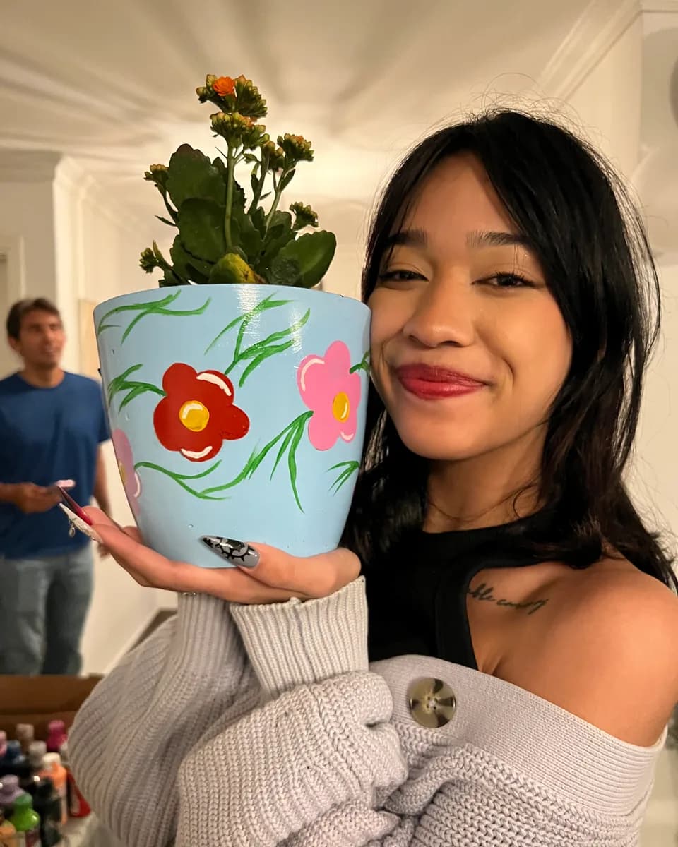 Participante sonríe con su maceta pintada a mano con flores rojas y su planta